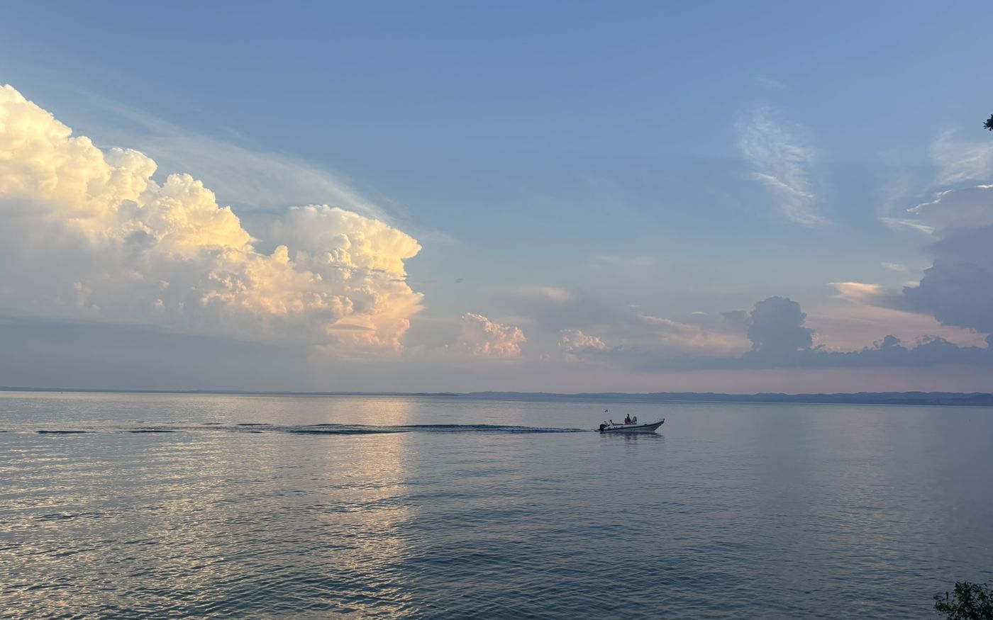 Lake Garda in the evening, a small motorboat leaving a long trail under towering clouds